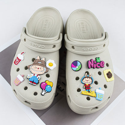 Beige clogs with colorful decorative labubu shoe charms pins on a white background