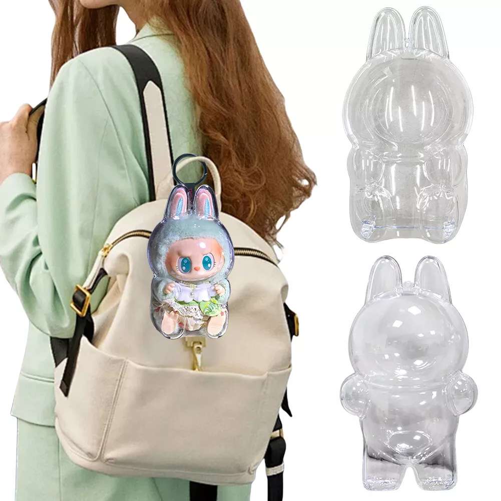 labubu Clear bunny-shaped backpack accessory attached to a beige backpack with a person wearing a light green jacket.