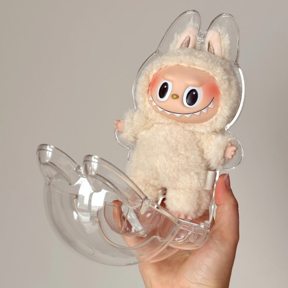 labubu Plush toy with large eyes in a clear plastic holder held by a hand against a neutral background