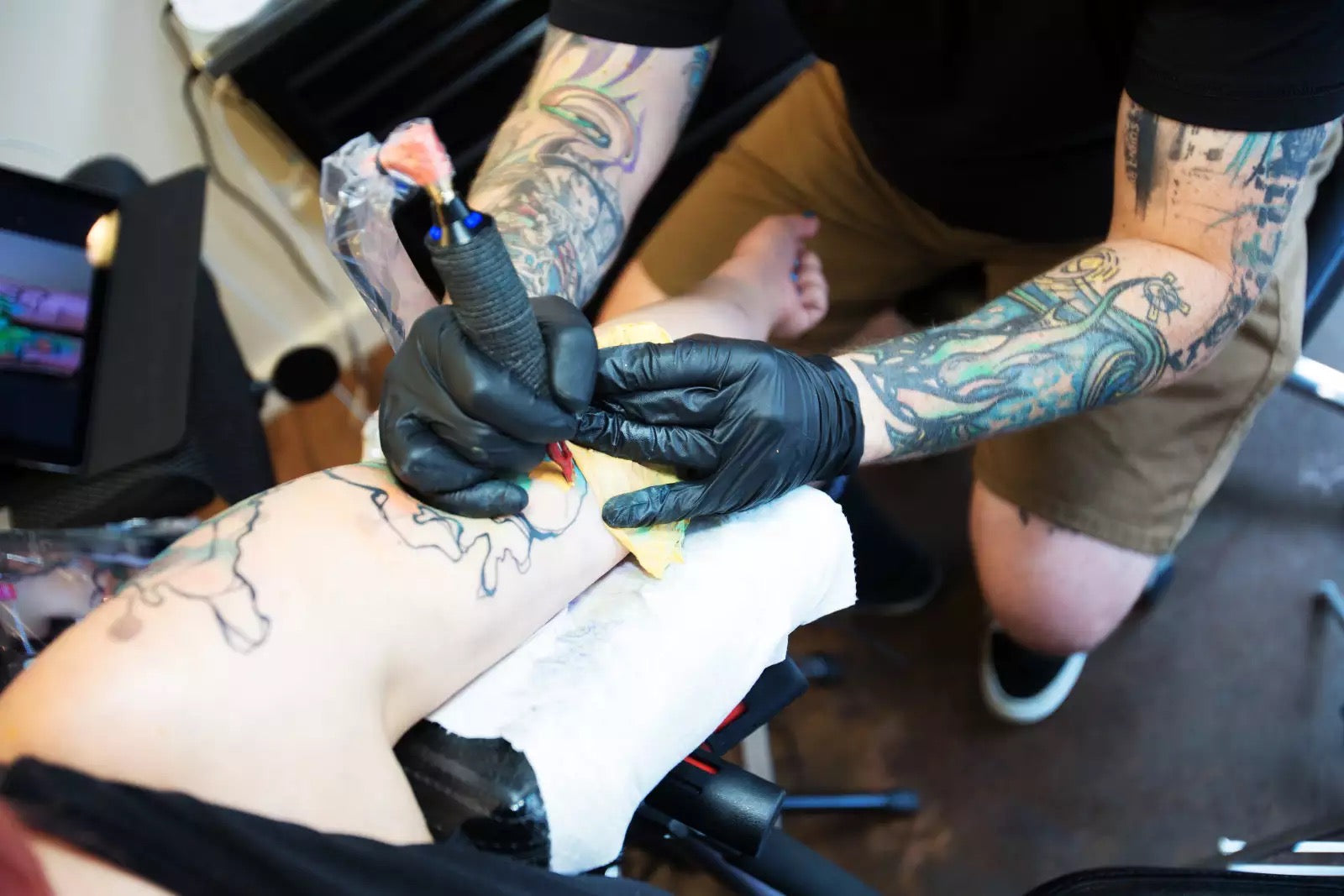 Tattoo artist wearing a pair of black nitrile gloves working on a tattoo with a colorful design.